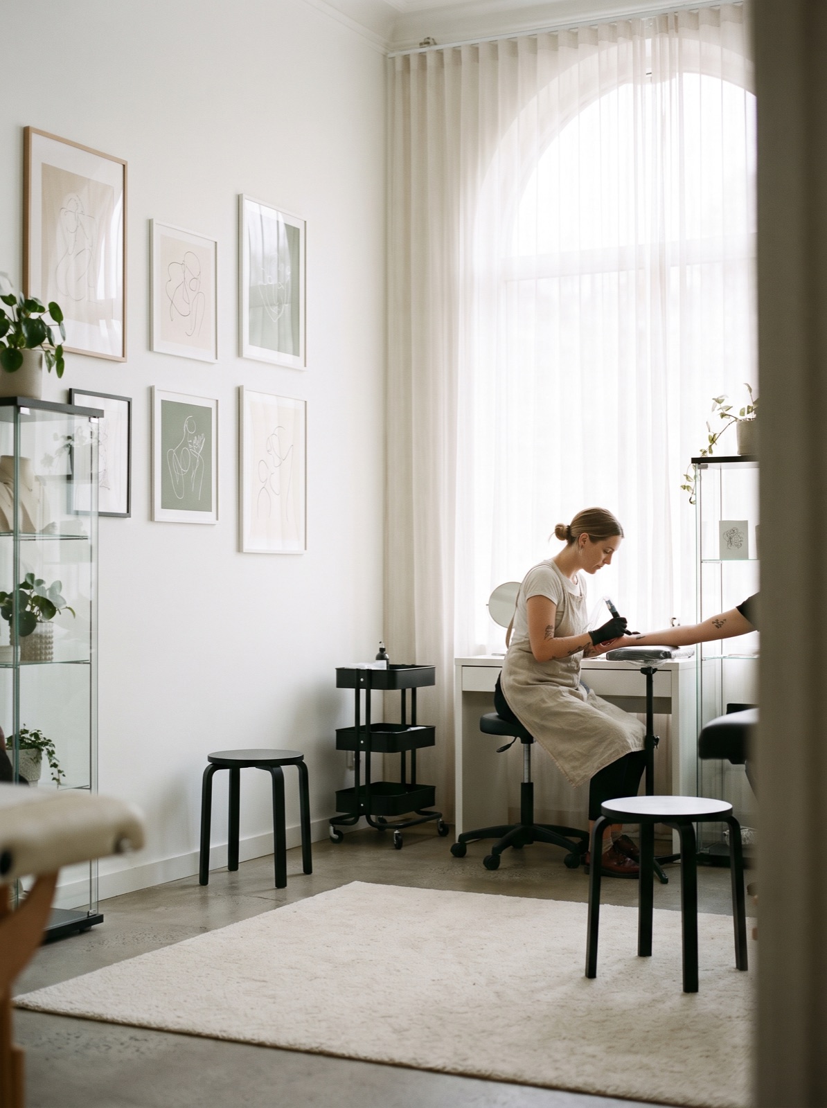 A tattoo artist working at a clean white station beside a window inside the bright, minimalist Zaycheza Studio