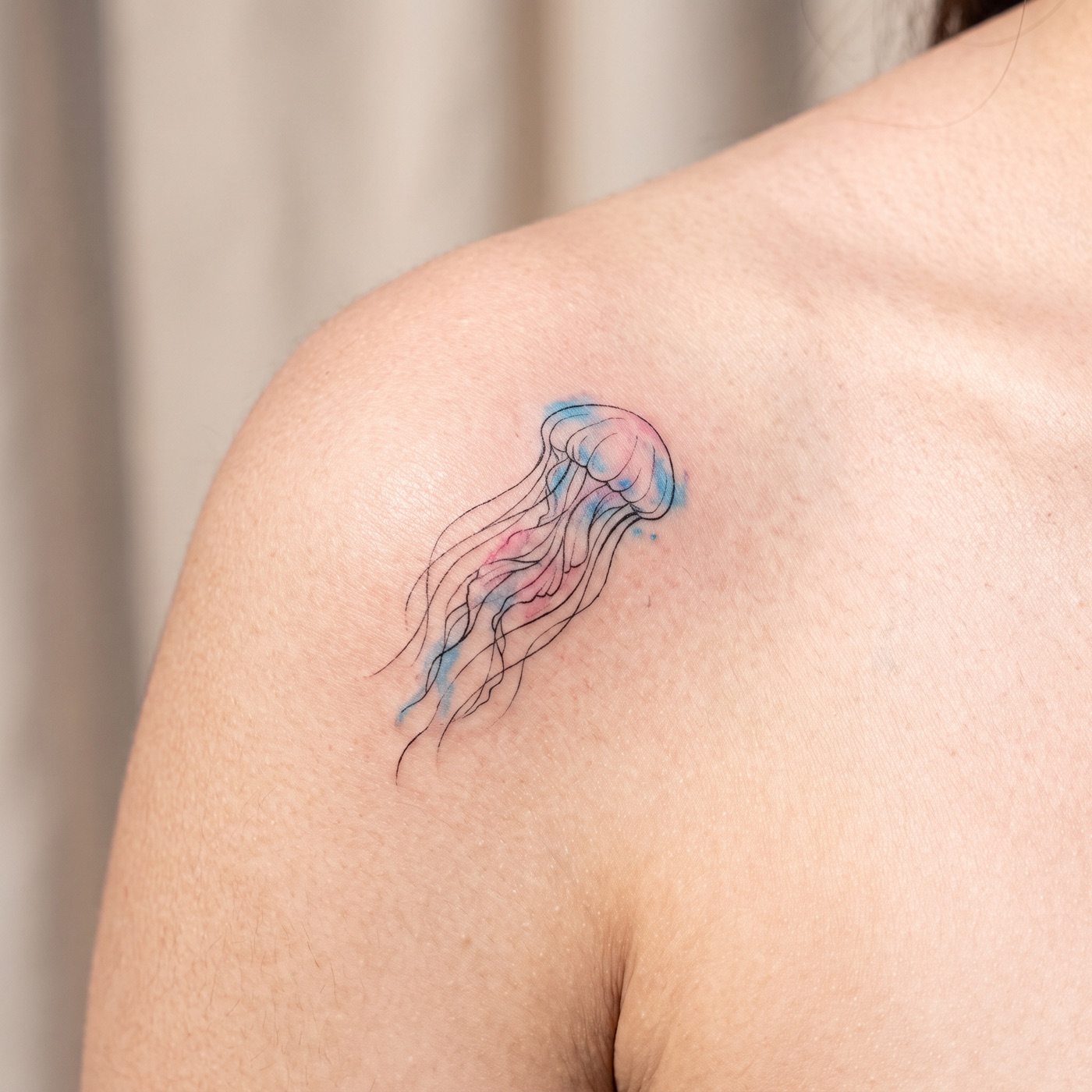 Delicate fine-line jellyfish tattoo with a pale color wash on a shoulder